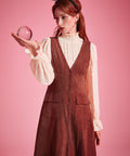Woman wearing rust brown A-line button front jumper dress layered over cream blouse