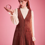Woman wearing rust brown A-line button front jumper dress layered over cream blouse