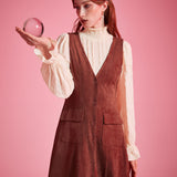 Woman wearing rust brown A-line button front jumper dress layered over cream blouse