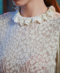 Close-up of ivory floral lace blouse with smocked cuff and layered ruffle trim