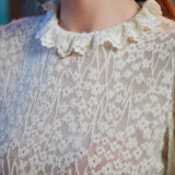 Close-up of ivory floral lace blouse with smocked cuff and layered ruffle trim