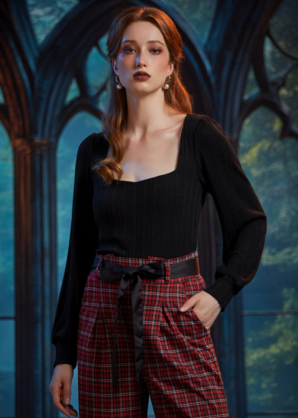 Woman wearing fitted black square neck top tucked into high-waisted red plaid trousers with black bow belt
