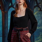 Woman wearing fitted black square neck top tucked into high-waisted red plaid trousers with black bow belt
