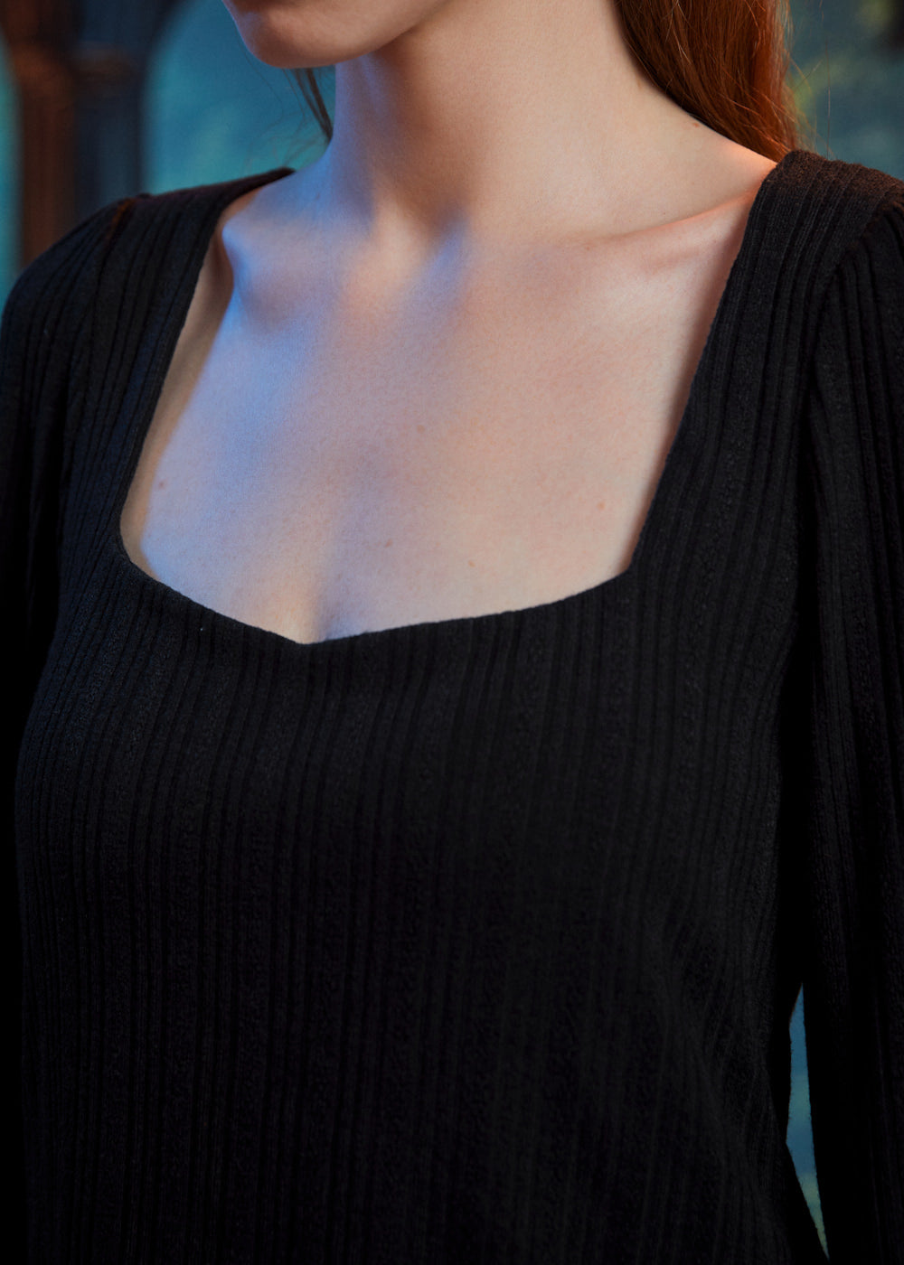 Close-up of woman wearing black ribbed knit top showing the wide square neckline and textured fabric