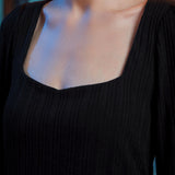 Close-up of woman wearing black ribbed knit top showing the wide square neckline and textured fabric