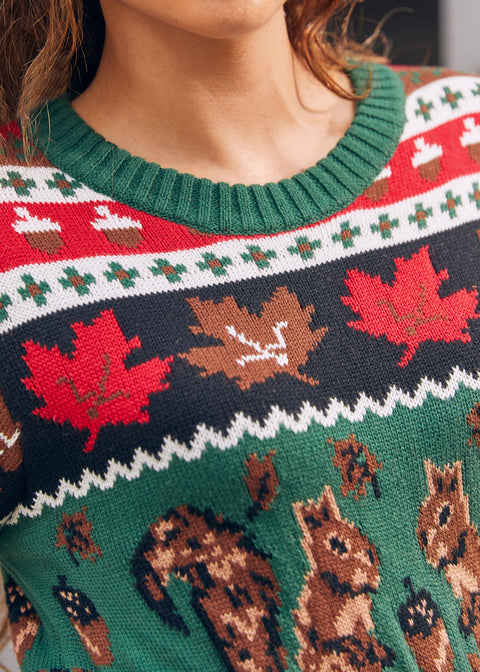 Close-up of a festive knit sweater with a green crew neck and a holiday pattern featuring red maple leaves, acorns, and brown squirrels.