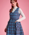 Woman wearing a navy and aqua plaid button-front jumper dress with her hand in an oversized patch pocket