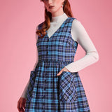 Woman wearing a navy and aqua plaid button-front jumper dress with her hand in an oversized patch pocket