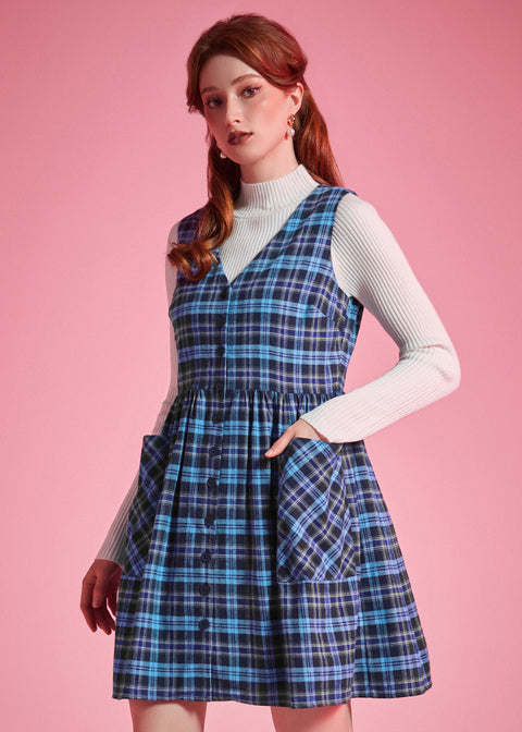 Woman wearing a navy and aqua plaid button-front jumper dress with her hand in an oversized patch pocket