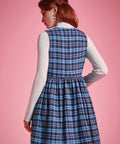 Back view of woman wearing a blue plaid sleeveless jumper dress showing fitted bodice, gathered waist and flared skirt