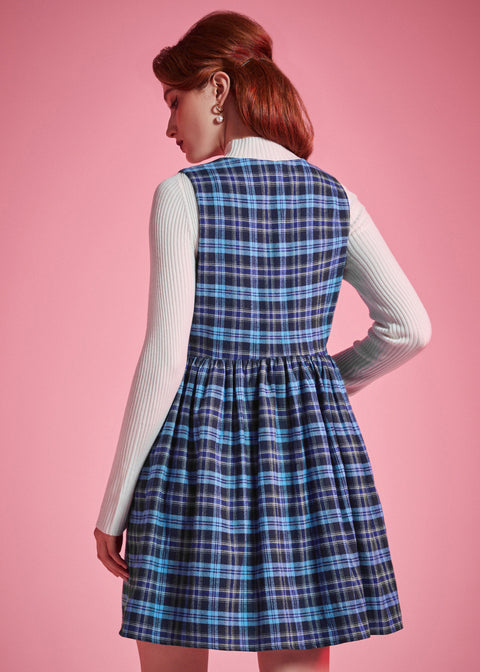 Back view of woman wearing a blue plaid sleeveless jumper dress showing fitted bodice, gathered waist and flared skirt
