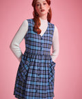 Portrait of woman wearing the Prep School Blues plaid jumper dress layered over a white ribbed mockneck sweater