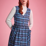 Portrait of woman wearing the Prep School Blues plaid jumper dress layered over a white ribbed mockneck sweater