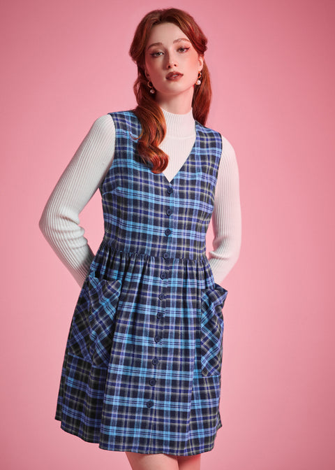 Portrait of woman wearing the Prep School Blues plaid jumper dress layered over a white ribbed mockneck sweater
