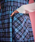 Close-up of woman placing her hand in the bias-cut patch pocket of a blue plaid button-front jumper dress