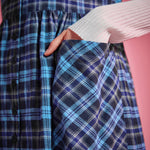 Close-up of woman placing her hand in the bias-cut patch pocket of a blue plaid button-front jumper dress