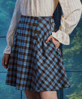 Three-quarter view of woman wearing blue brown plaid flare skirt with her hand in the side pocket, showing bias-cut side panel