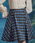 Woman wearing a blue and brown plaid high-waisted A-line skirt with double sailor-style buttons and flared side panels