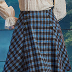 Woman wearing a blue and brown plaid high-waisted A-line skirt with double sailor-style buttons and flared side panels