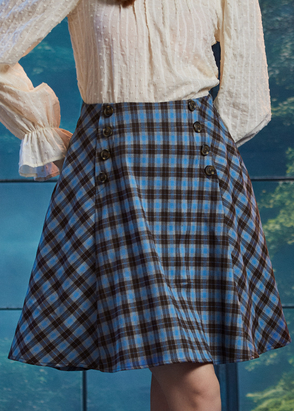 Woman wearing a blue and brown plaid high-waisted A-line skirt with double sailor-style buttons and flared side panels