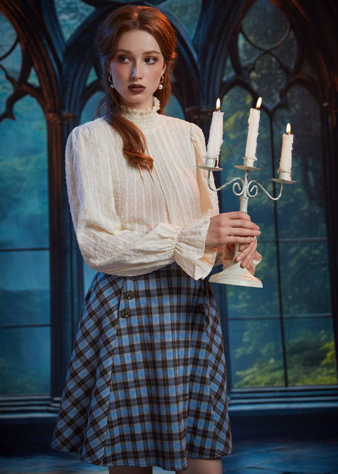 Woman wearing the ModCloth Sailor Flare blue plaid skirt with ivory high-neck blouse while holding a lit three-candle candelabra