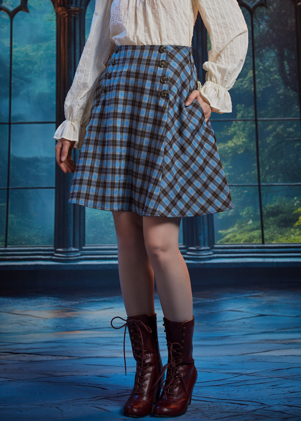 Woman wearing a high-waisted blue and brown plaid A-line skirt with side pocket, decorative buttons and burgundy boots