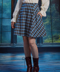 Woman wearing a high-waisted blue and brown plaid A-line skirt with side pocket, decorative buttons and burgundy boots