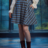 Woman wearing a high-waisted blue and brown plaid A-line skirt with side pocket, decorative buttons and burgundy boots