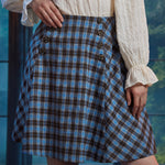 Front angled close-up of woman wearing a vintage-inspired plaid A-line skirt with double rows of sailor-style buttons
