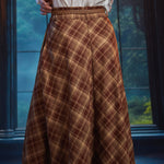 Back view of woman wearing a brown and tan plaid midi skirt showing sweeping A-line silhouette and braided belt