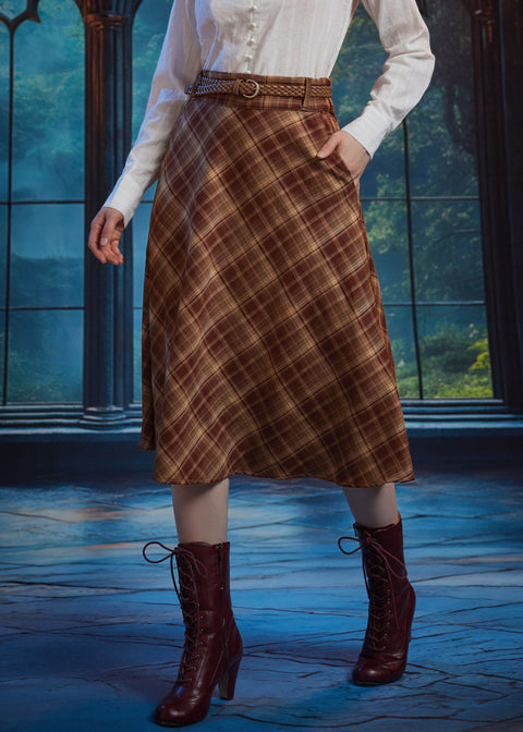 Woman wearing brown plaid A-line midi skirt with braided belt and hand in side pocket, styled with white blouse and boots