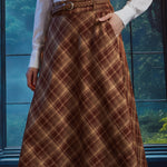 Woman wearing a brown plaid high-waisted midi skirt with braided belt, A-line silhouette and hand in side pocket
