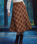Woman wearing a vintage-inspired brown plaid A-line midi skirt with braided waist belt and burgundy lace-up boots