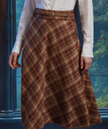 Front close-up of woman wearing the Brown Study plaid midi skirt showing diagonal bias-cut plaid and braided belt