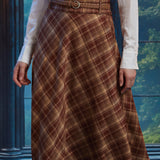 Front close-up of woman wearing the Brown Study plaid midi skirt showing diagonal bias-cut plaid and braided belt