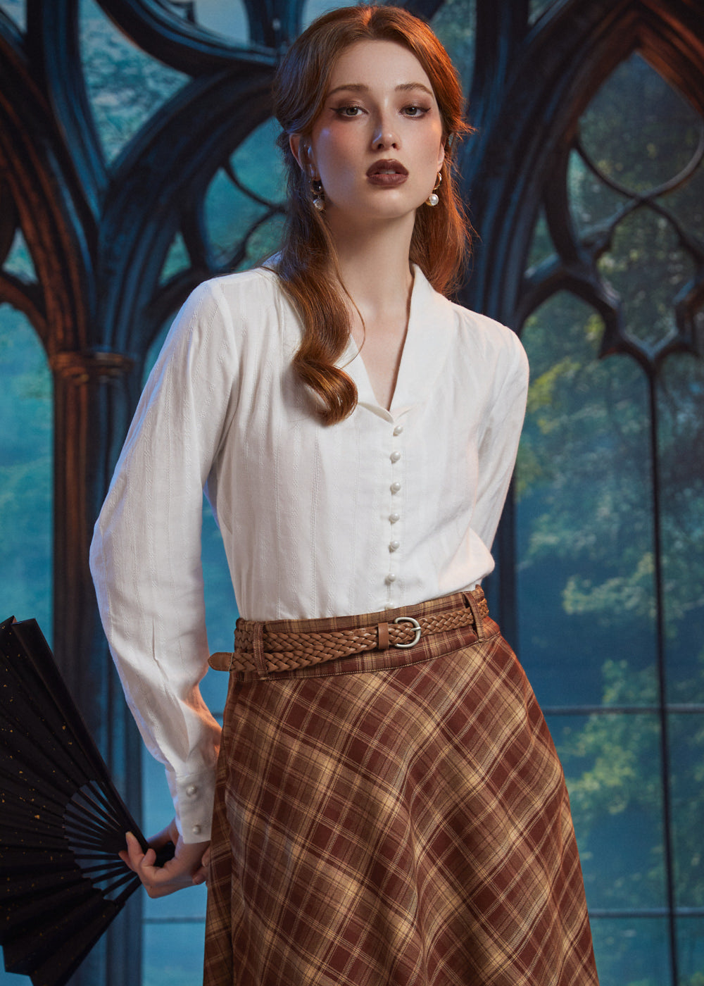 Woman wearing an ivory pearl button blouse with shawl collar and long sleeves, styled with a brown plaid skirt and braided belt