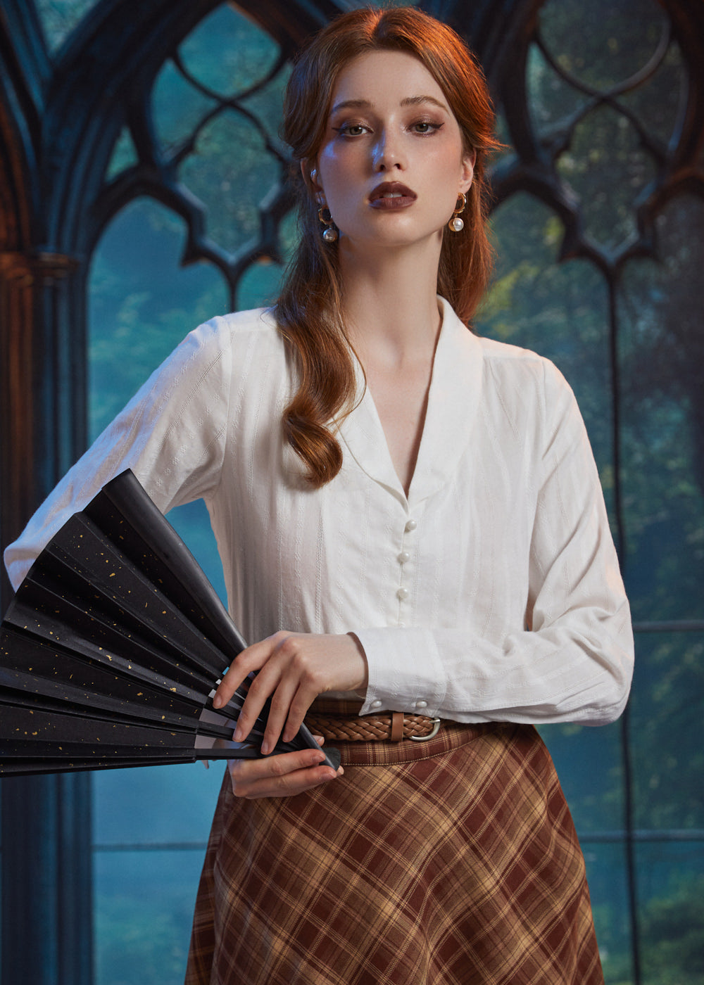 Woman wearing ivory shawl collar blouse with pearl-style buttons while holding a black folding fan