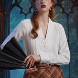 Woman wearing ivory shawl collar blouse with pearl-style buttons while holding a black folding fan
