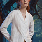 Three-quarter view of woman wearing ivory pearl button blouse showing V-neck shawl collar, long sleeves and dobby stripe texture