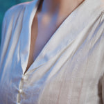 Close-up of ivory cotton blend blouse showing shawl collar, V-neckline, pearl-style buttons and vertical dobby stripe texture