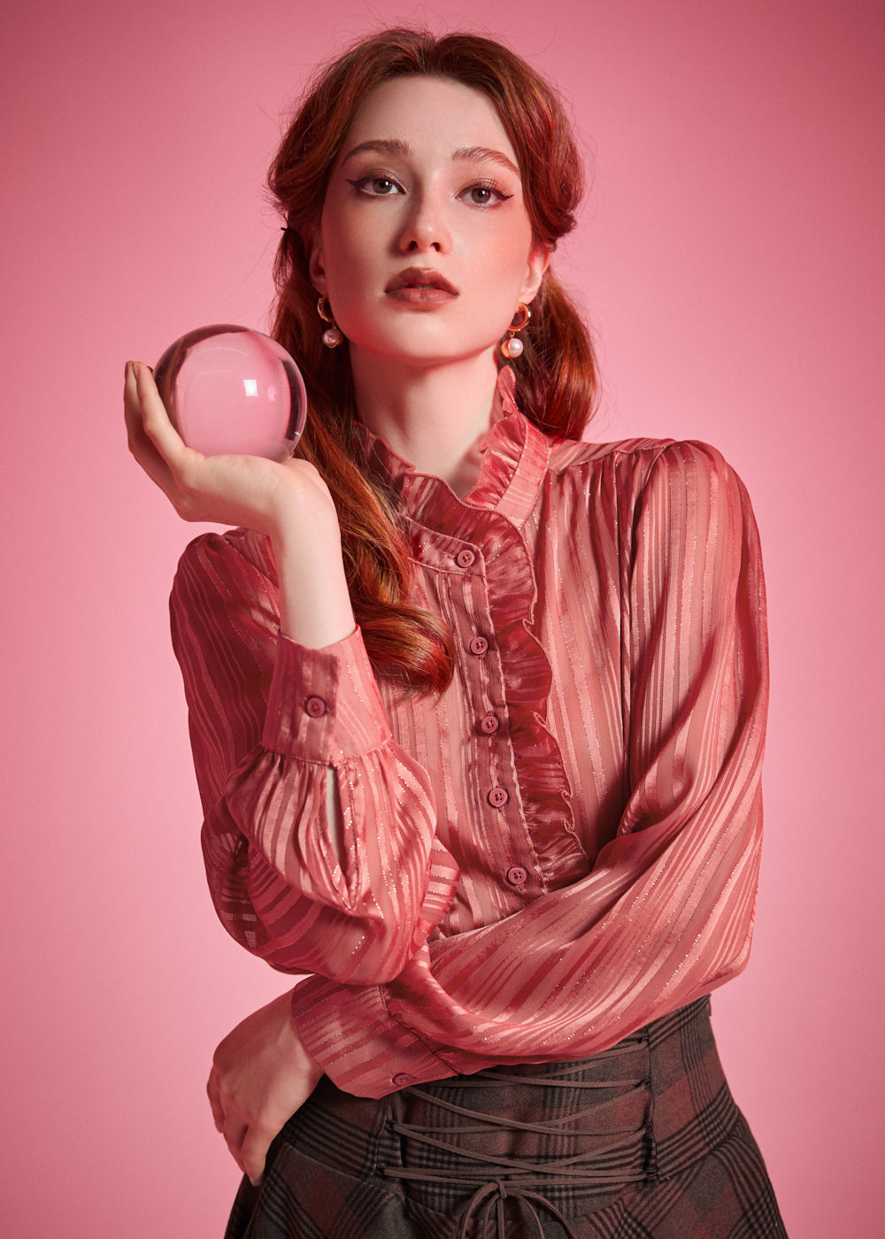 Woman wearing dusty rose high neck ruffle blouse while holding a glass sphere, showing the striped sheer fabric and button front