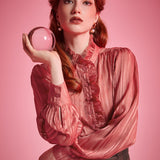 Woman wearing dusty rose high neck ruffle blouse while holding a glass sphere, showing the striped sheer fabric and button front