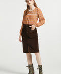 Full-length woman wearing brown floral blouse styled with brown corduroy midi skirt and ankle boots