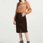 Full-length woman wearing brown floral blouse styled with brown corduroy midi skirt and ankle boots