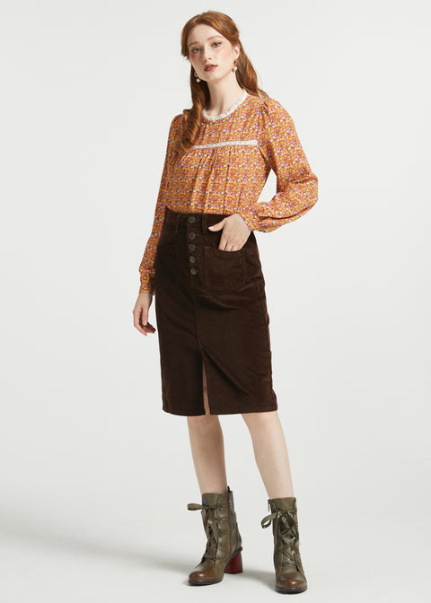 Full-length woman wearing brown floral blouse styled with brown corduroy midi skirt and ankle boots