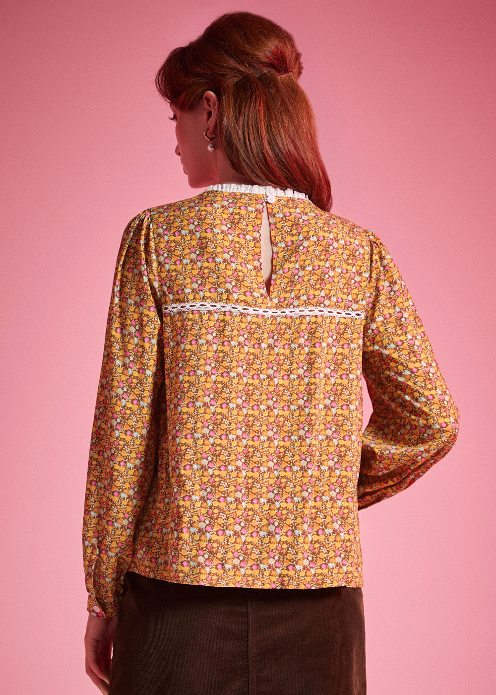 Back view of woman wearing brown floral blouse with white lace yoke trim and keyhole closure