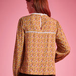 Back view of woman wearing brown floral blouse with white lace yoke trim and keyhole closure