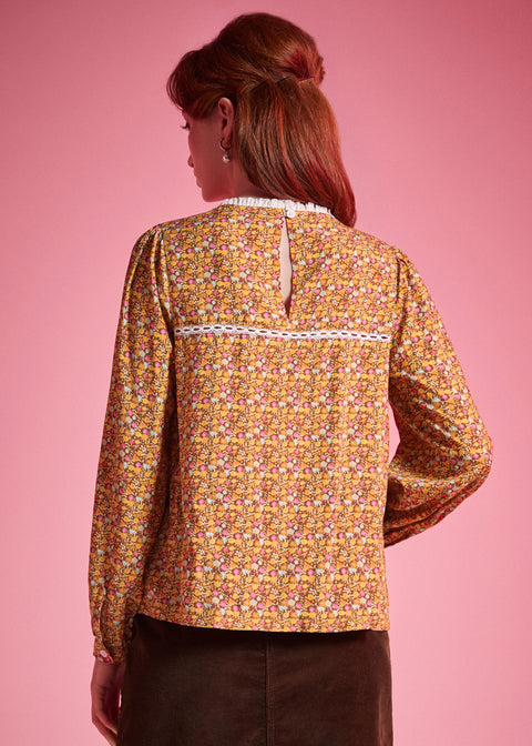 Back view of woman wearing brown floral blouse with white lace yoke trim and keyhole closure