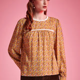 Front view of woman wearing brown floral long sleeve blouse with white lace neckline and gathered yoke