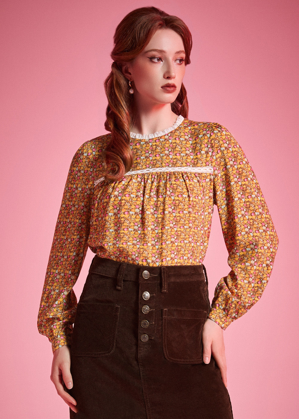Woman wearing brown floral prairie blouse with lace trim and long sleeves against pink background